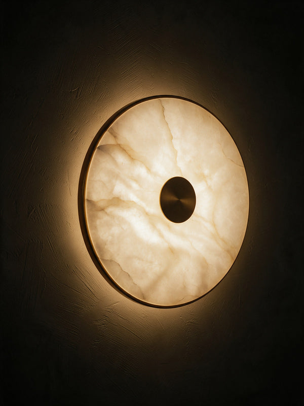 A round alabaster disc wall light with a brass centre on a dark plaster wall