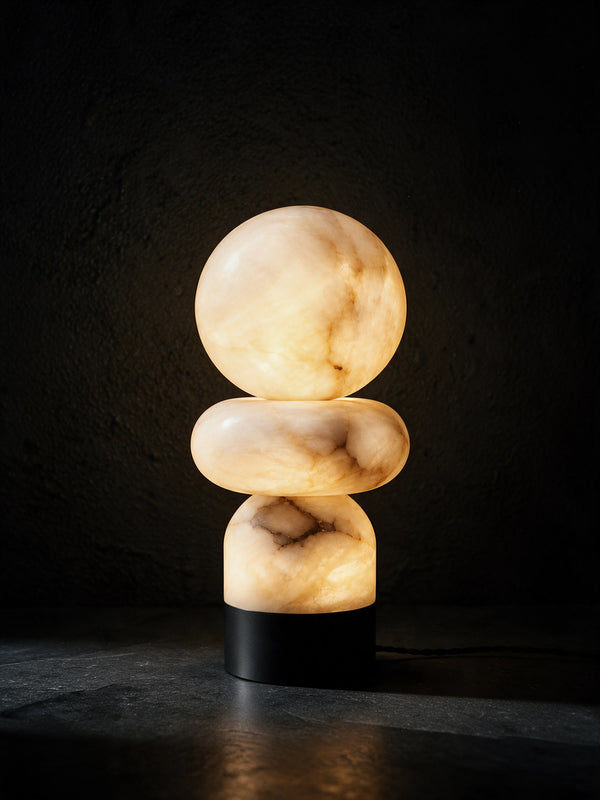 A stacked alabaster table lamp glowing on dark stone